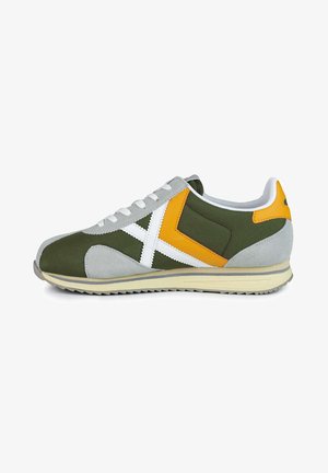 Zapatilla verde y gris con acentos en blanco y amarillo, parte superior de textil, superposiciones de ante, cuello acolchado y suela de goma con textura en el dibujo.