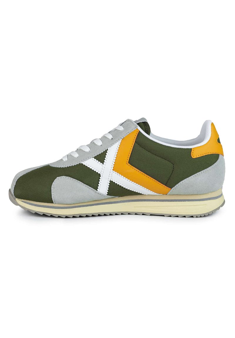 Zapatilla verde y gris con acentos en blanco y amarillo, parte superior de textil, superposiciones de ante, cuello acolchado y suela de goma con textura en el dibujo.
