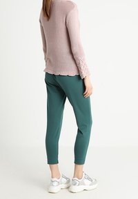 Ljust rosa texturerad tröja med volangkant, matchad med gröna smalare byxor och vita sneakers med silverdetaljer.