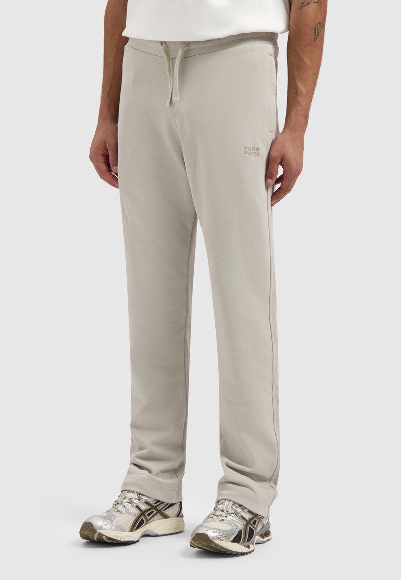Lichtbeige sweatpants met een trekkoord in de taille, rechte pijpen, zijzakken en een klein logo gedrukt op het linkerbeen. Zacht katoenen materiaal.