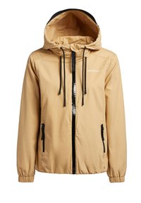 Chaqueta beige con capucha, cremallera negra, cordones negros, puños elásticos y bolsillos laterales con cremallera, diseñada para uso casual.