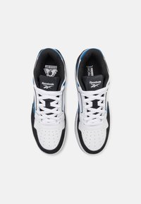 Baskets blanches avec des accents en daim noir et des détails bleus. Dotées d'un bout perforé, de lacets plats et d'une languette avec logo. Semelle en caoutchouc.