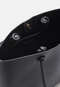 Mustan nahkatote-bag, jossa on sileä pinta, pyöreä pohja ja napitus. Sisäpuolella on etiketti ja pehmeä vuori.