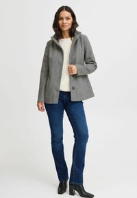 Veste en mélange de laine grise avec un col haut et quatre boutons, associée à un jean bleu foncé et des bottines à talons blocs noires.