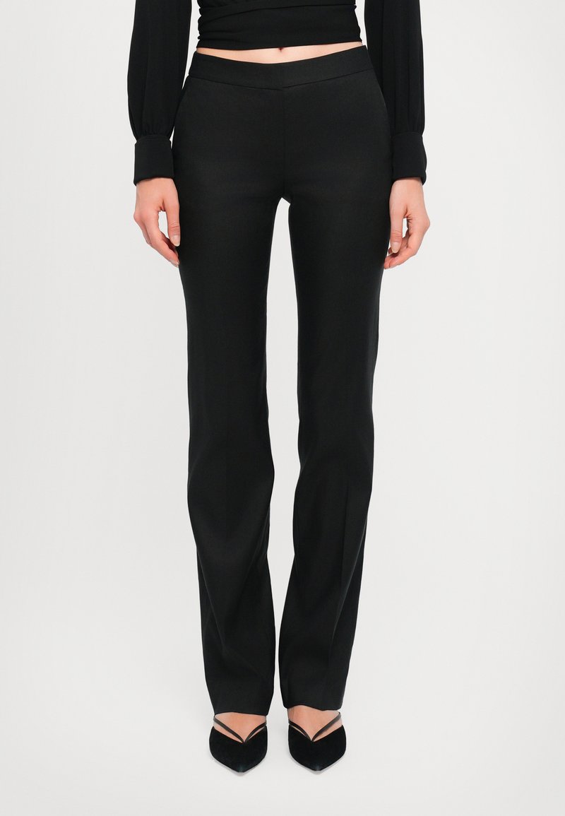 Pantalons noirs ajustés avec une texture lisse, coupe slim et design à jambe droite, avec une taille mi-haute. Associés à des escarpins à bout pointu.