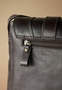 Brown leather bag with a textured surface, featuring a zippered closure and decorative stitching on the flap and body.