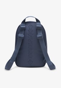 Σακίδιο πλάτης σε ναυτικό μπλε, κατασκευασμένο από ανθεκτικό ύφασμα, με ρυθμιζόμενους ιμάντες και ανάγλυφο κείμενο "Converse" μπροστά. Μινιμαλιστικός σχεδιασμός.