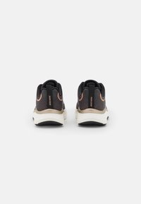 Black athletic shoes with a textured upper, contrasting rose gold accents, and a cushioned white midsole. Brand logo on heel.