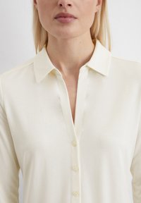 White button-up shirt featuring a collar, long sleeves, and a slightly textured fabric. The front has a placket with light-colored buttons.