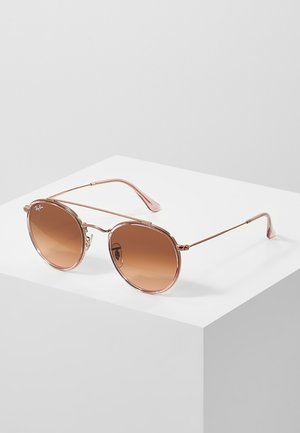 Occhiali da sole rotondi con montatura in metallo rosa oro, lenti gradienti marroni e aste sottili. Presentano un delicato dettaglio del logo sul lato.