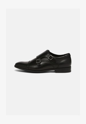 Zapatos de cuero negro con punta afilada, acentos de doble hebilla y un diseño elegante. Presentan un tacón bajo y apilado y una textura superficial suave.
