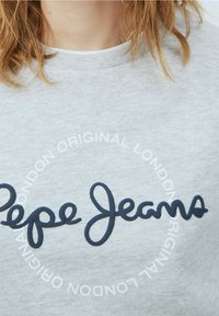 Felpa grigia con un logo "Pepe Jeans" blu navy in evidenza, circondato da un motivo testuale circolare bianco. Texture morbida e design casual.