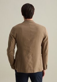 Blazer marrone chiaro realizzato in tessuto texturizzato, con una vestibilità su misura, spacco posteriore singolo e polsini con bottoni. Design minimalista senza motivi visibili.