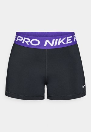 Crne atletske kratke hlače s ljubičastim elastičnim pojasom s natpisom "NIKE PRO." Imaju mali bijeli Nike logotip u donjem lijevom kutu.