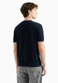 Pull en maille bleu marine à manches courtes et col rond. Texture lisse et design ajusté, associé à un jean gris clair. Style minimaliste.