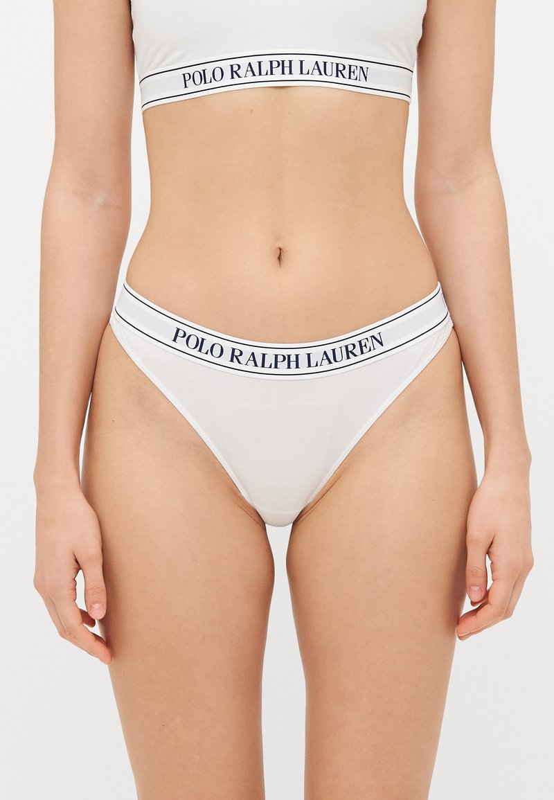 Bēšas kokvilnas stringveida apakšveļa ar platu jostasvietu, uz kuras ir izšūts "POLO RALPH LAUREN" tumši zilā krāsā. Gluda tekstūra, minimāls dizains un zemu jostasvietu.