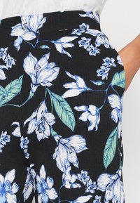 Tissu à motifs floraux noir, présentant des fleurs bleues et blanches avec des feuilles vertes. Surface texturée avec une finition côtelée.