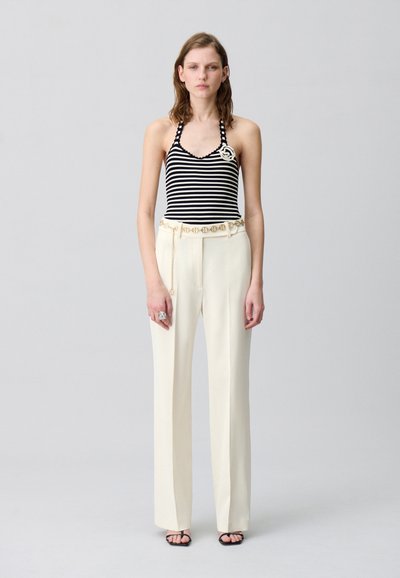 Top a halter a righe bianche e nere abbinato a pantaloni larghi color crema, accentuato da una cintura a catena e da una spilla decorativa sul top.
