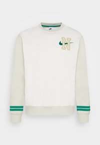 Ljust beige sweatshirt med kontrasterande gröna ränder på muddar och nederkant. Har en broderad gul "N" och grön Nike-logga på bröstet.