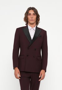 Burgundy double-breasted suit with black satin lapels, featuring a pocket square and a slim-fit design. Textured fabric, contrasting button details.