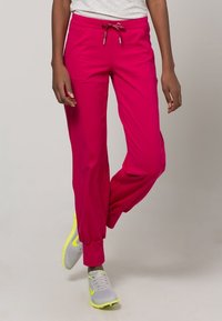 Roze sportieve joggerbroek met trekkoord in de taille, taps toelopende boorden en zijzakken, gecombineerd met grijze en neongele sneakers.