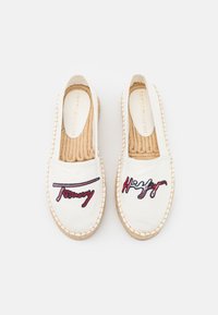 Białe espadryle Tommy Hilfiger z konopnymi podeszwami i haftowaną nazwą marki w czerwonym i niebieskim na górze, widok z góry.