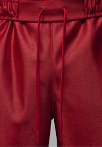 Pantalon en tissu texturé rouge avec une ceinture élastique et des cordons visibles à l'avant au centre.