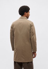 Barna, középhosszú kabát strukturált gallérral és hosszú ujjakkal, sima anyagból készült, egyenes szabású, látható zárak nélküli.