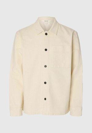 Chemise à manches longues de couleur crème avec col, boutons noirs sur le devant, et une poche poitrine unique sur le côté gauche.