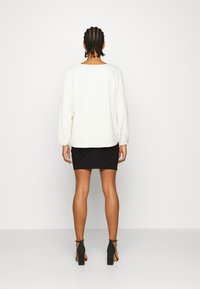 Blusa branca de mangas longas com mangas franzidas, combinada com uma saia mini preta justa. Sapatos de salto alto pretos completam o conjunto.