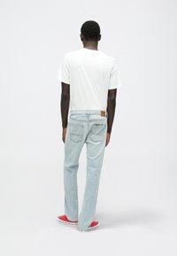 Jeans de mezclilla azul claro con un corte relajado, detalle de costura en los bolsillos traseros y una etiqueta de cuero marrón. Combinados con una camiseta blanca y zapatos rojos.