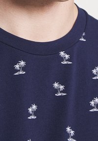 T-shirt in cotone blu navy con motivi di palme bianchi ricamati, colletto rotondo e maniche corte, che mostra una texture liscia.