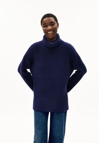 Navyfarbener, gerippter Strickrollkragenpullover mit lässiger Passform. Verfügt über abfallende Schultern und lange Ärmel. Kombiniert mit blauen Jeans.