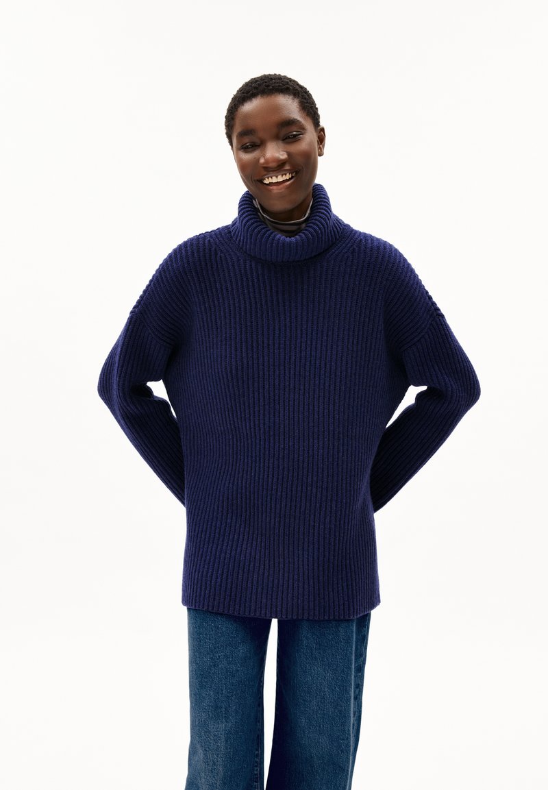 Navyfarbener, gerippter Strickrollkragenpullover mit lässiger Passform. Verfügt über abfallende Schultern und lange Ärmel. Kombiniert mit blauen Jeans.