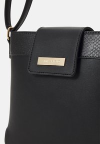 Borsa a tracolla nera in pelle sintetica liscia, con accenti in stampa serpente testurizzata e una targhetta logata in metallo dorato sul risvolto anteriore.