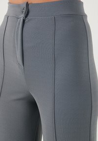 Gray high-waisted pants with a textured fabric, featuring a button closure, front pleats, and side pockets for functionality.