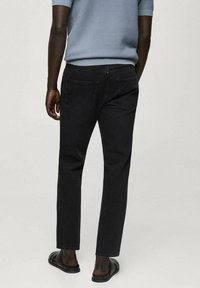 Blugi negri din denim cu o croială dreaptă, design cu cinci buzunare și detalii subtile de cusătură. Purtați cu sandale negre, văzuți din spate.