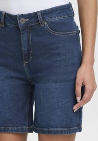 Denimshorts i mörkblått med hög midja, prydda med standardfickor, knäppning fram och synliga sömnadsdetaljer på sömmarna.