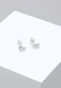 Srebrne naušnice s dugmetima s dva sferna elementa, sa glatkom površinom i minimalističkim dizajnom, postavljene na svijetloj pozadini.