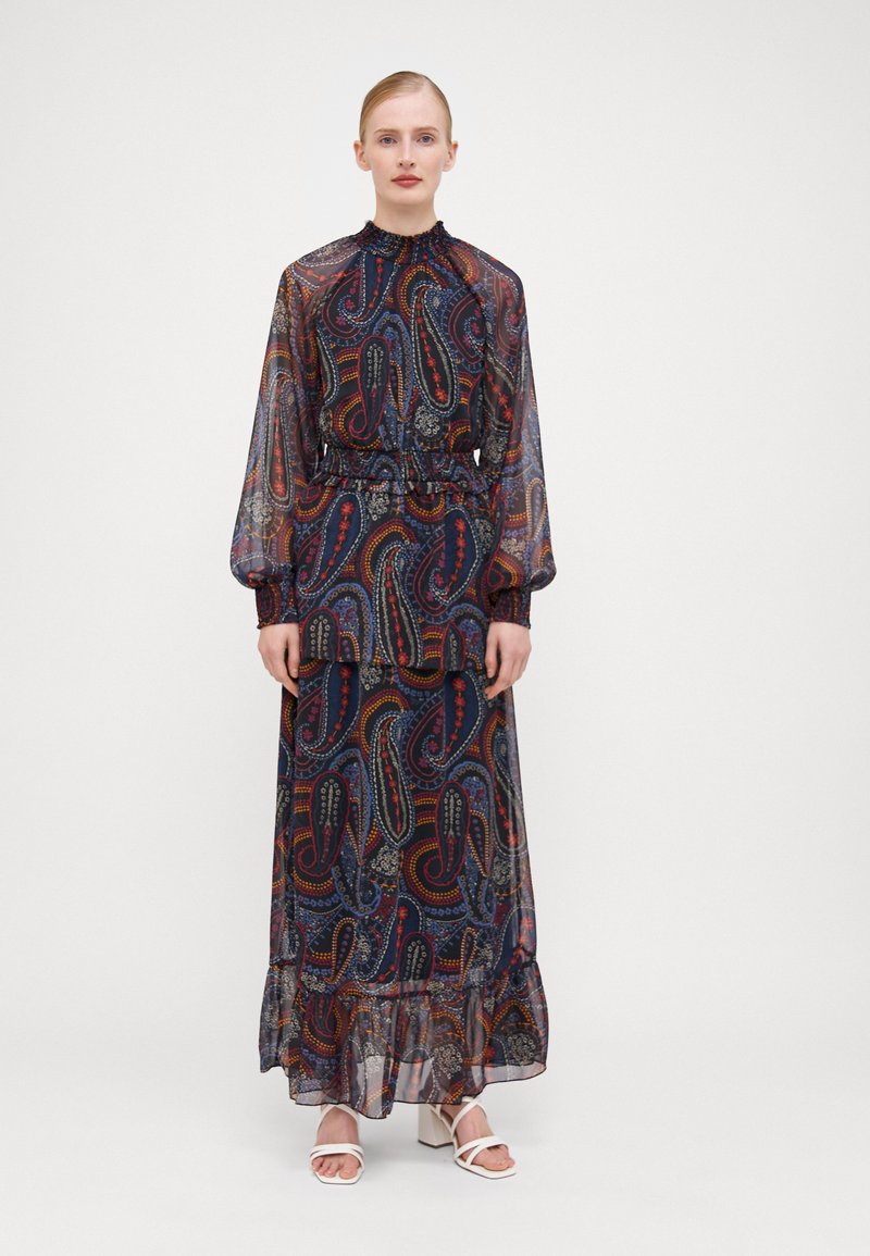 Μακρύ φόρεμα με σχέδιο από διάφανο ναυτικό ύφασμα με paisley σχέδια σε κόκκινο, κίτρινο και μπλε. Διαθέτει ψηλό λαιμό και ελαστική μέση με ριγέ τελείωμα.