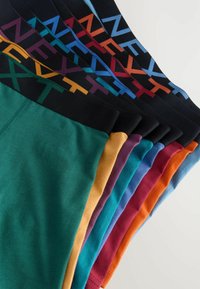 Stive de lenjerie de bumbac colorată strident, cu brâie elastice pe care apare cuvântul "NEXT" în diverse culori îndrăznețe.