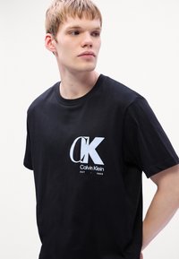 Mustapaita, jossa on näyttävä valkoinen logo "CK" ja tekstit "Calvin Klein EST 1968", pyöreä kaula-aukko ja lyhyet hihat.