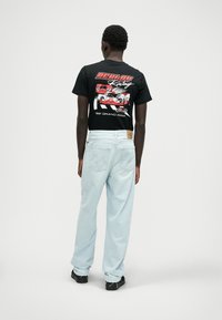 Svart grafisk t-skjorte med racingdesign, sammen med lyseblå baggy jeans. Jeansene har klassisk fem-lommers stil og synlig søm.