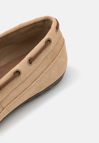 Beige boat shoe featuring a textured fabric upper with a herringbone pattern, brown laces, and a black rubber sole.