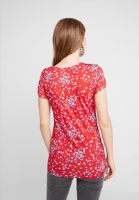 Camisa roja de manga corta con un estampado floral en azul y blanco. Tela suave, cuello redondo y un diseño ajustado que llega hasta la mitad de la cadera.