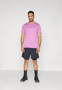 Camiseta deportiva morada jaspeada, pantalones cortos negros, calcetines negros y zapatillas de correr. El conjunto presenta un ajuste ceñido y la marca Nike en la camiseta.