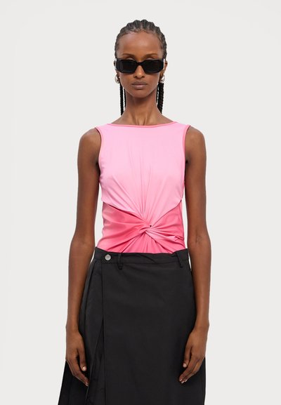 Pink sleeveless top with a knotted front detail, paired with a black skirt featuring a side slit and button accent. Flat background.