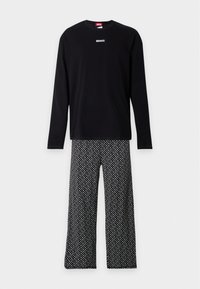 Chemise noire à manches longues avec petit logo Diesel blanc, associée à un pantalon large à motifs noir et blanc sur fond uni.