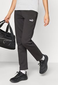 Μαύρο παντελόνι φόρμας PUMA με εφαρμοστή γραμμή και ελαστική ζώνη μέσης. Συνδυάζεται με μαύρα αθλητικά παπούτσια και μαύρη τσάντα duffle. Απλή λεπτομέρεια λογότυπου.