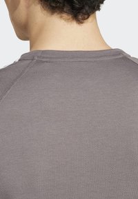 Camisa de manga corta en gris claro con escote redondeado y mangas raglán. Textura de tela suave con detalles de costura sutiles.